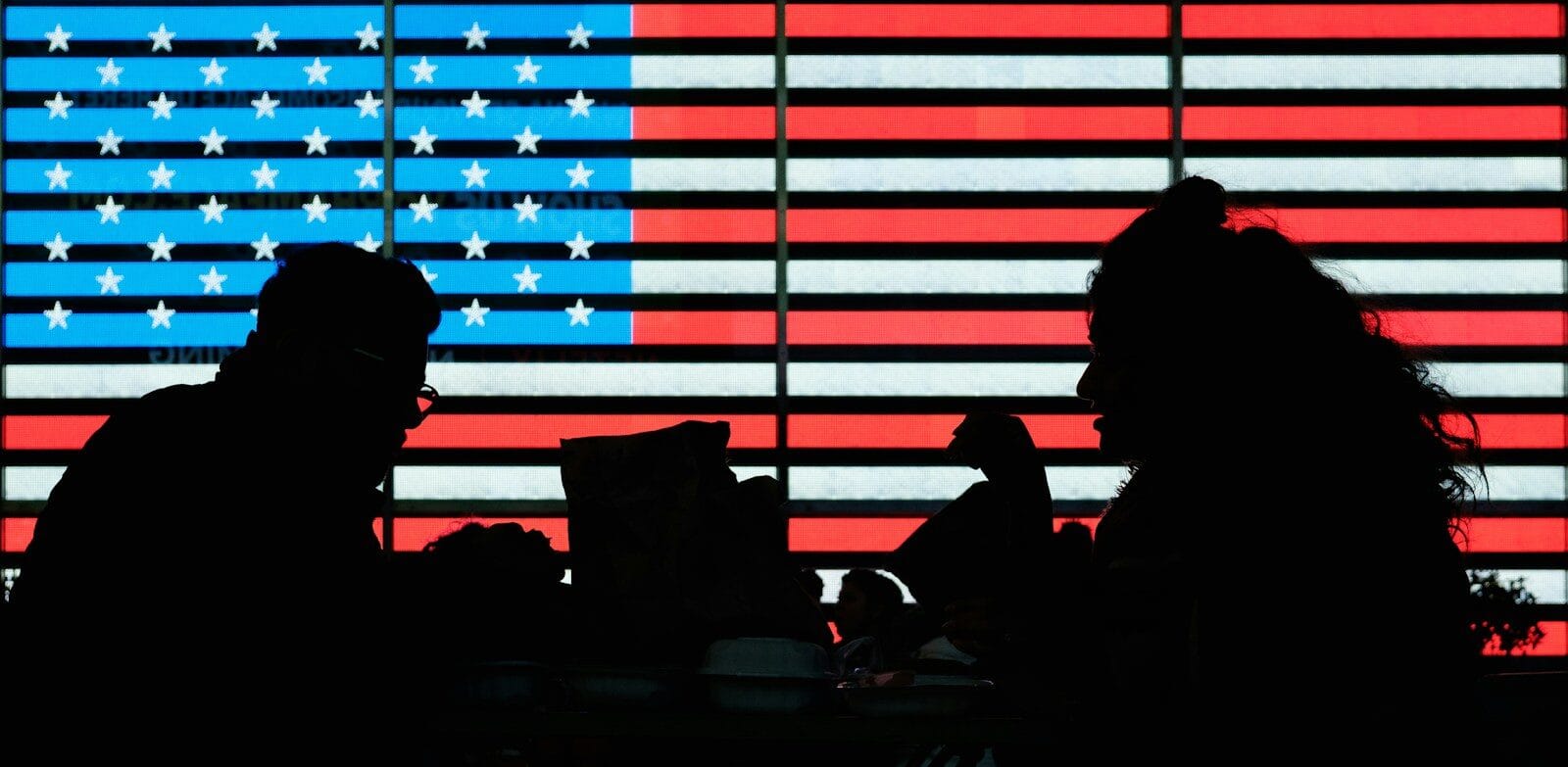 silhouette of people gathered in front of lighting in the pattern of an American flag