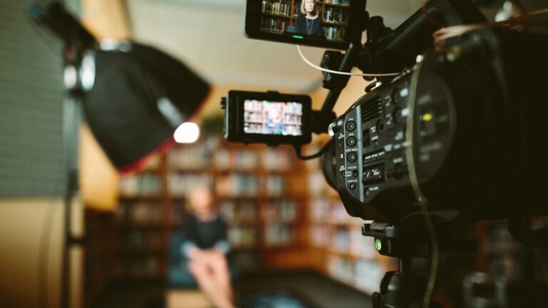 a camera aimed at a person sitting in front bookshelf