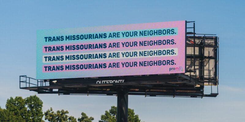 A billboard peeks above the treeline in St. Louis Missouri. The background is a blue to pink gradient. The text reads 4 times over "Trans Missourians are your neighbors"