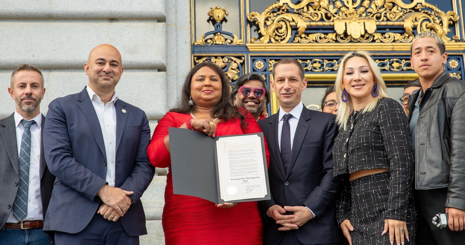   Anjali Rimi, flanked by San Francisco city officials and supporters, holds a signed proclamation of Transgender Immigrants Day on November 18, 2025. Photo by Pax Ahimsa Gethen, CC BY-SA 4.0.  