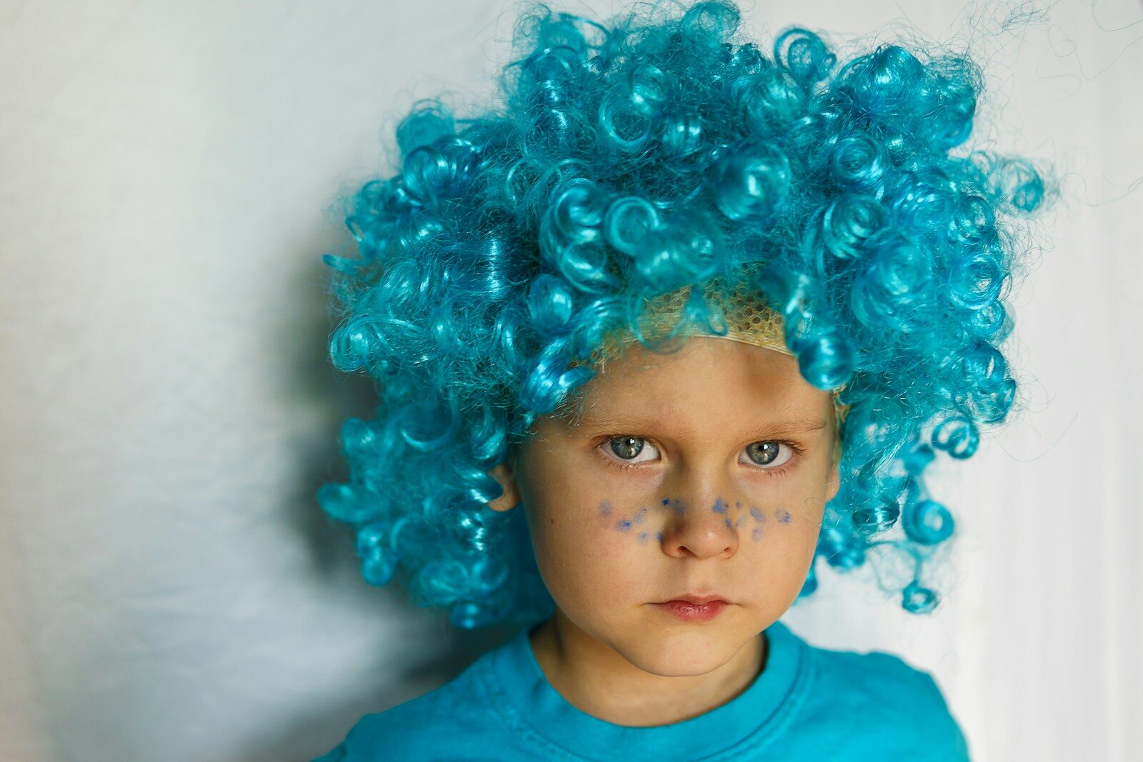 child in blue crew neck shirt with bright curly aqua wig glares at camera
