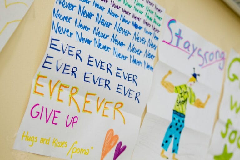a photo of a child's drawing on a hospital wall featuring a man in a muscle pose and the words stay strong never ever ever ever (etc) give up